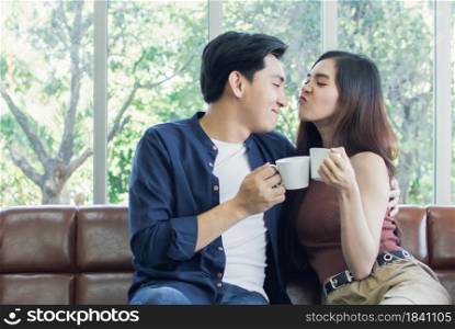Couple is holding cups of coffee and sitting in living room in the morning