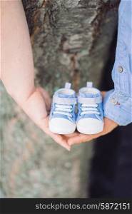 Couple is holding hands and tiny baby shoes