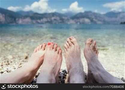 Couple is holding their feet in the crystal clear water, summer holiday