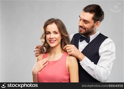 couple, jewelry and people concept - happy man puts necklace with diamond pendant on his girlfriend over grey background. happy man puts necklace on his girlfriend