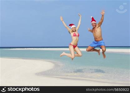 Couple Jumping On Beach Wearing Santa Hats