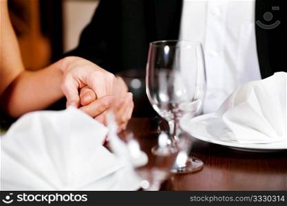 Couple, just hands to be seen, is holding hand while waiting for their food and drinks in a restaurant