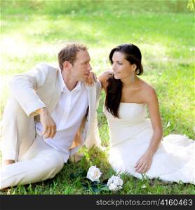 couple just married sitting in park green grass with white rose