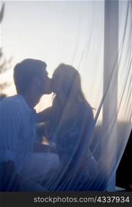 Couple kissing behind veil outdoors
