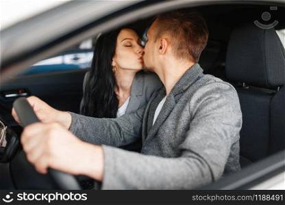 Couple kissing in new car, showroom. Male and female customers buying vehicle in dealership, automobile sale, auto purchase