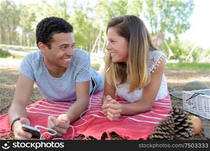 couple laughing as they share earphones to listen to smartphone