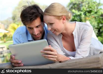 Couple laying on deck chair with electronic tablet