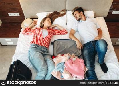 Couple lies on the bed with opened suitcase, top view. Fees on journey concept. Luggage preparation. Couple lies on bed with opened suitcase, top view