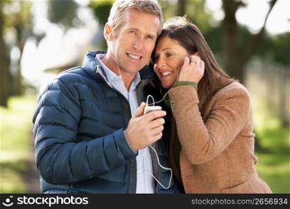 Couple Listening To MP3 Whilst Walking In Autumn Park