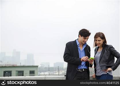 Couple listening to shared earplugs on city rooftop