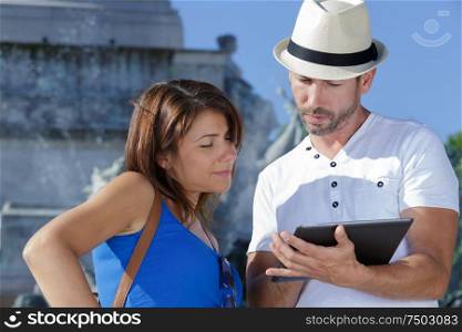 couple looking at digital tablet by fountain