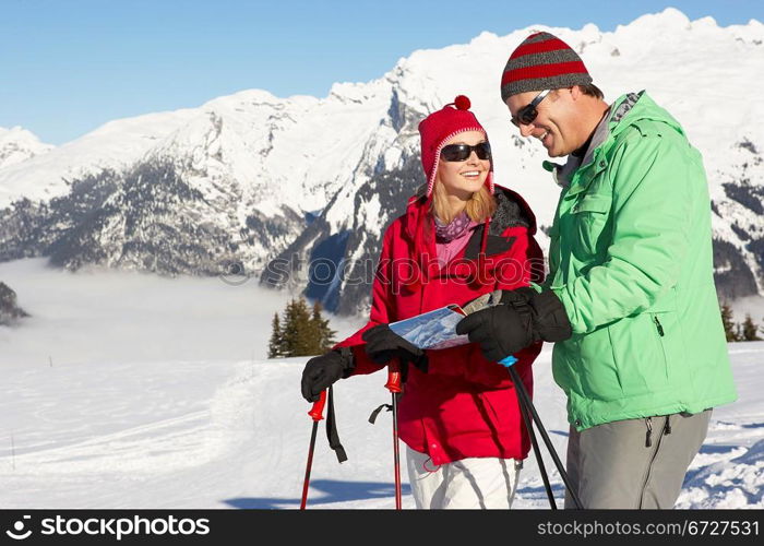 Couple Looking At Map Whilst On Ski Holiday In Mountains