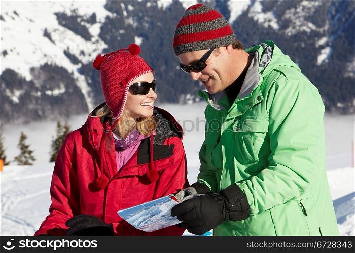 Couple Looking At Map Whilst On Ski Holiday In Mountains