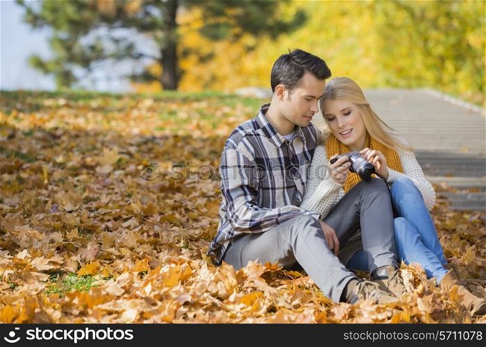 Couple looking at pictures on digital camera in park during autumn