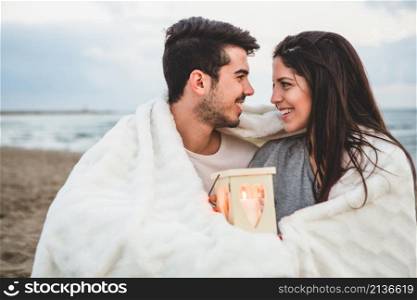 couple looking each other sand with candle blanket