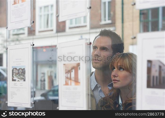 Couple Looking in Real Estate Agent&acute;s Window
