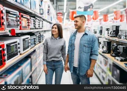Couple looking on shelf with electric ovens in a supermarket. Customers in shop, family choosing consumer goods