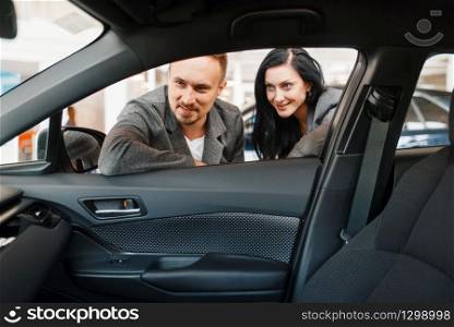 Couple looks on interior of the new car in showroom. Male and female customers buying vehicle in dealership, automobile sale, auto purchase