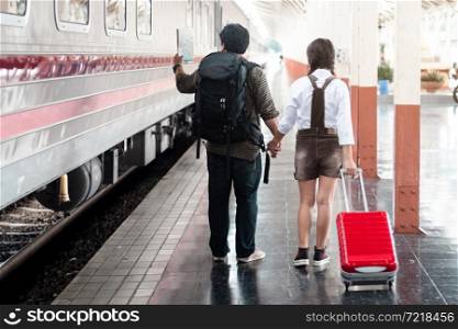 Couple lovers tourist Hold hands with each other hold a map in at in a train station carrying her trolley red bag,traveler with backpack in summer Holiday concept Thailand