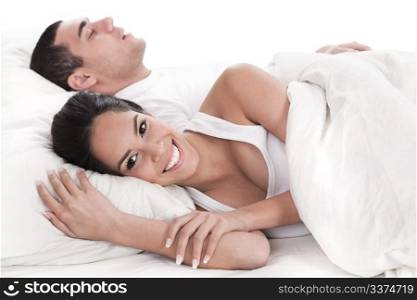 Couple lying in bed together, man sleeping and woman smiling cover in white sheet