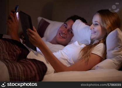 Couple Lying In Bed Using Digital Tablet And Mobile Phone