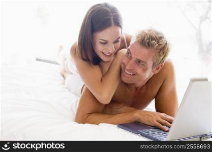 Couple lying in bed with laptop smiling