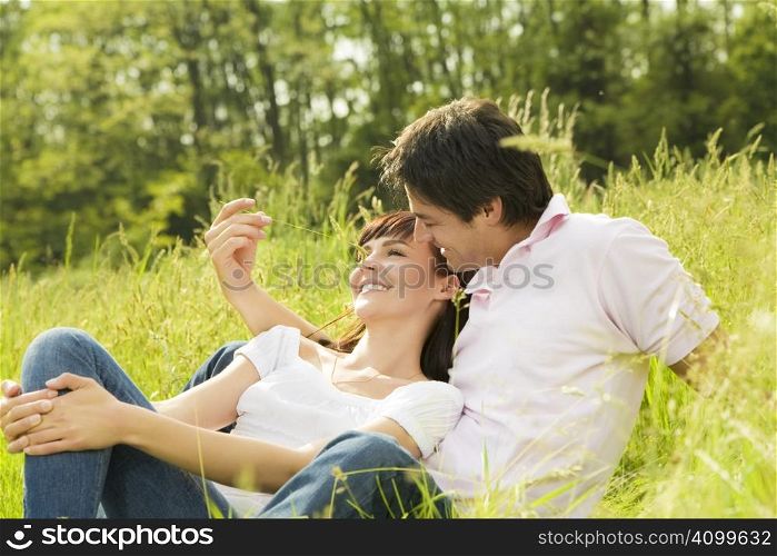 Couple lying in grass, man tickling her girlfriend&acute;s nose and smiling