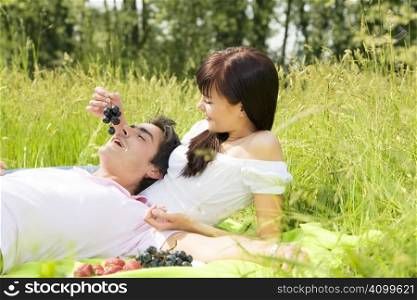 Couple lying in grass, smiling and eating grapes