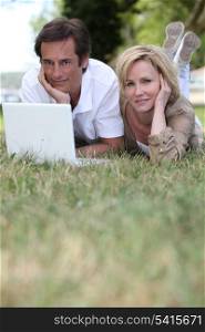 couple lying in grass using laptop