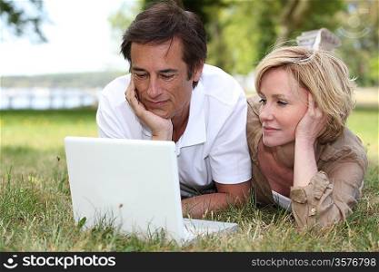 Couple lying in the grass looking at a laptop