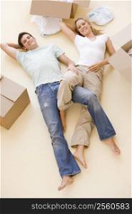 Couple lying on floor by open boxes in new home smiling