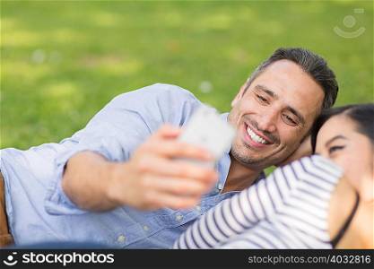Couple lying on grass using smartphone to take selfie