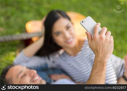Couple lying on grass using smartphone to take selfie