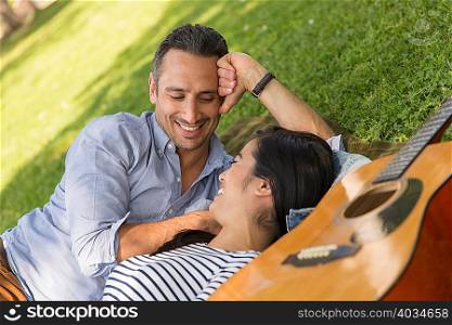 Couple lying on grass with acoustic guitar smiling