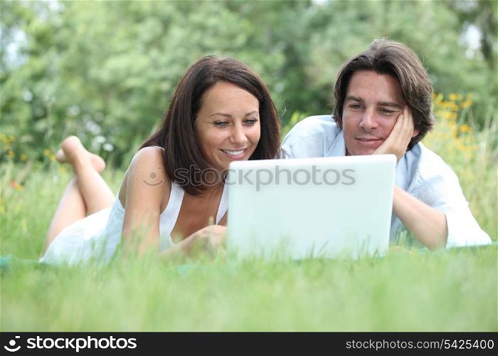 Couple lying on the grass looking at a laptop computer screen