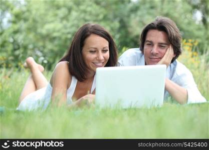 Couple lying on the grass looking at a laptop computer screen