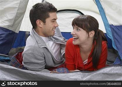 Couple lying side by side in tent, laughing