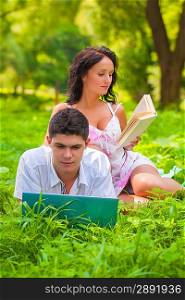couple lying with laptop and book at park
