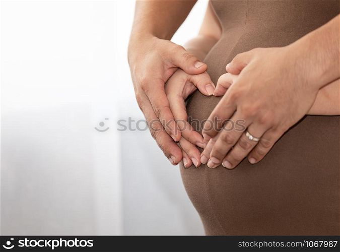 couple making a heart shape on a pregnant belly with family baby love care concept close up and selective focus