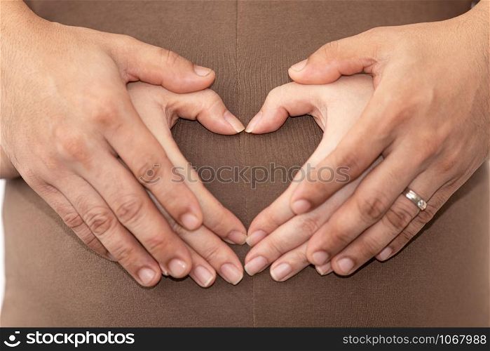 couple making a heart shape on a pregnant belly with family baby love care concept close up and selective focus