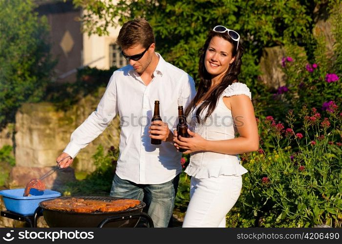 Couple - man and woman - doing the barbeque together in their garden in summer