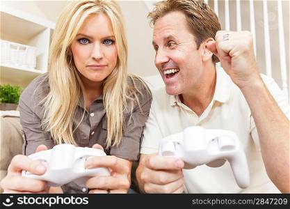 Couple, man and woman, having fun playing video console games together. The man has just beaten the woman, he is celebrating, she is annoyed.