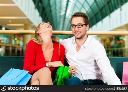 Couple - man and woman - in a shopping mall with colorful bags, they are checking what exactly they do have bought, she is surprised
