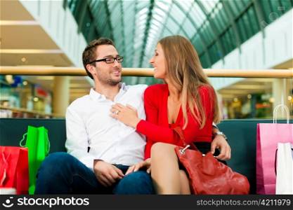 Couple - man and woman - in a shopping mall with colorful bags; they having a break
