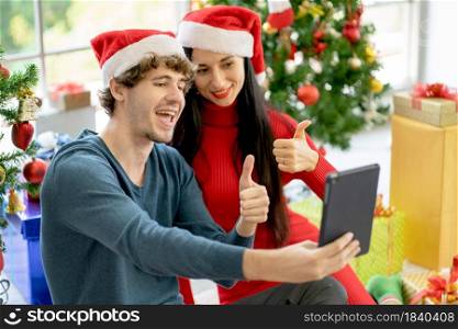 Couple man and woman show thumbs up to online chat via tablet during Christmas festival and they celebrate together and other people with new normal lifestyle.