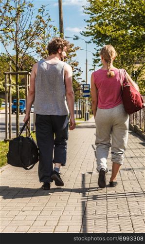 Couple man and woman with sport gym bags walking outdoor. Active young girl and guy in training suit sportswear.. Couple man and woman walking with sport bags.