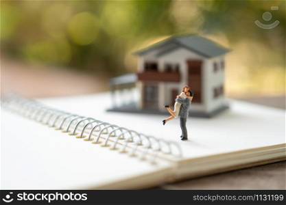 Couple Miniature 2 people standing model with house model make family Feel happy.as background real estate and family concept with copy space.
