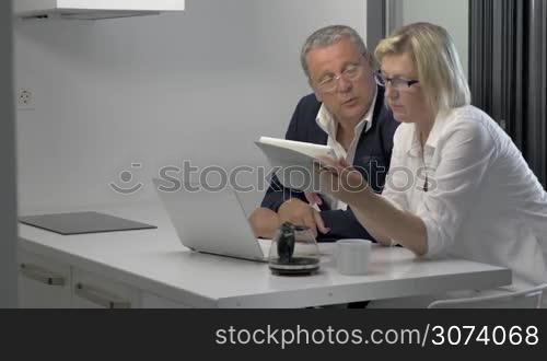 Couple of adults looking at tablet and talking in kitchen