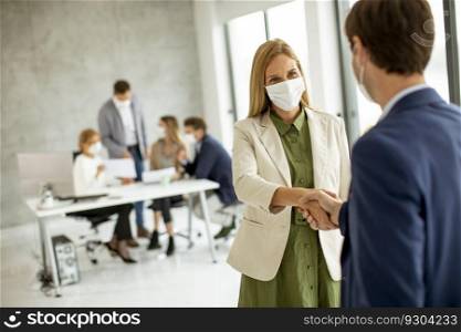 Couple of business people handshaking in the office and wearing protective face masks due to coronavirus epidemic
