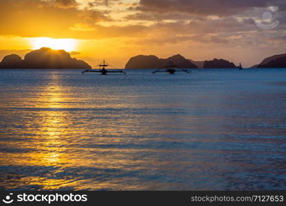 Couple of cruise philippinean bangca boats standing still on water with sunset and tropical islands in background, Palawan, Philippines